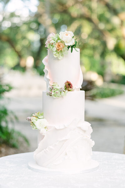 A stunning three-tier luxury wedding cake with delicate ruffled details and fresh floral accents, captured at an elegant wedding in Sarasota, Florida. Designed for a sophisticated celebration, this exquisite cake embodies timeless romance.