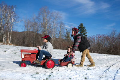 Three boys playing on toy tractor in snow | Family Photo Session Taken By Maine Photographer
