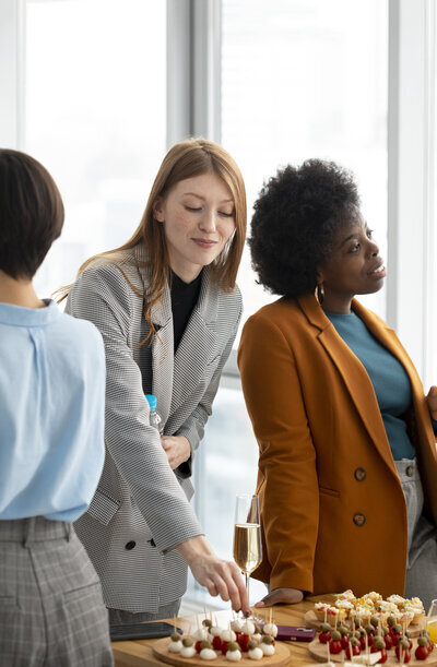 3 femmes picorant et discutant autour d'une table lors d'un cocktail pour un événement d'entreprise. Organisation d'événements Nantes Loire Atlantique Vendée.