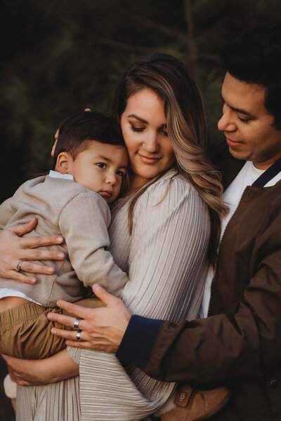 Mom holding son, and dad hugging from behind in Golden Hour