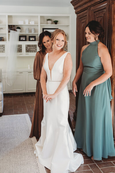 Wichita bride smiles shyly at the camera after getting ready with the help of her mother and bridesmaid