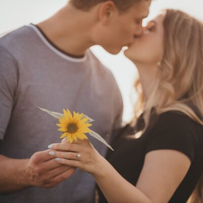 engagement photo of couple kissing while holding a flower