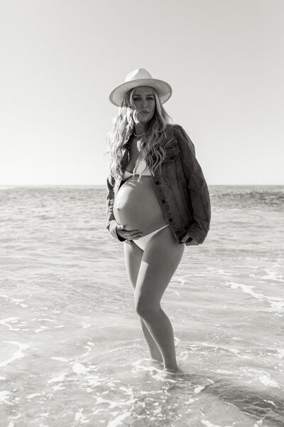 pregnant woman in denim and hat standing in the water