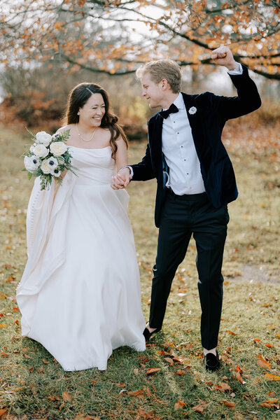 Bride and groom holding hands underneath autumn tree with orange leaves