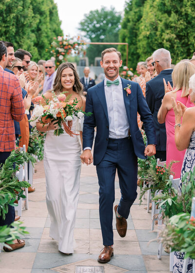 man in blue suit walking stylish bride back down the aisle after getting married and surrounded by friends