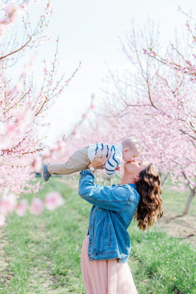 a mother kissing her baby surrounded by cherry blossom at high park