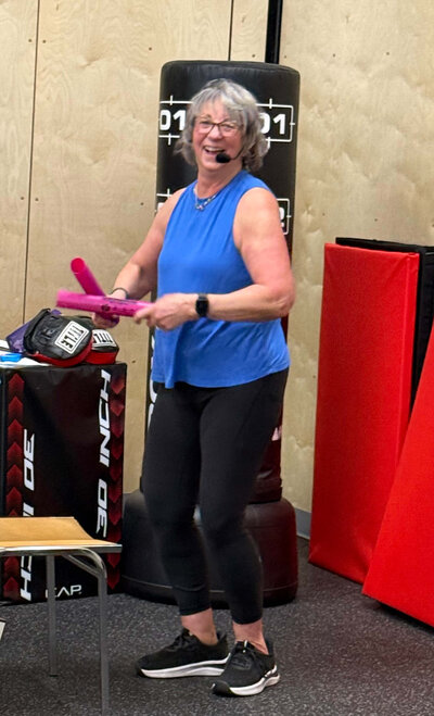 Coach Lori smiles and leads a Parkinson's exercise class in the Parkinson's Warriors Gym. 