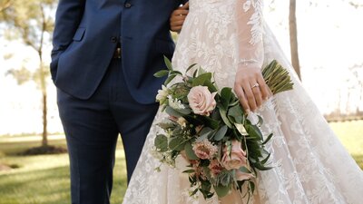 Husband and wife in wedding garb hold hands and bouquet
