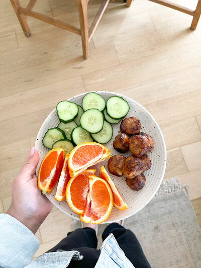 Image of above a plate of orange slices, cucumbers, and meatballs