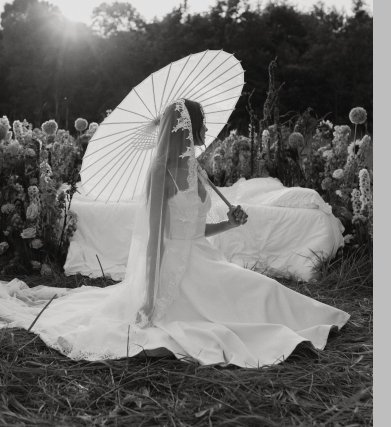 Women in a white dress sitting in the grass with an umbrella and the sun glistening