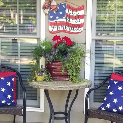Back patio with porch chairs and side table with plant and American flag wooden door hanger with God Bless America hand written