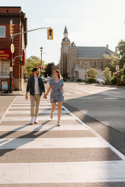 paris ontario engagement couple crosses street and holds hands as sun sets