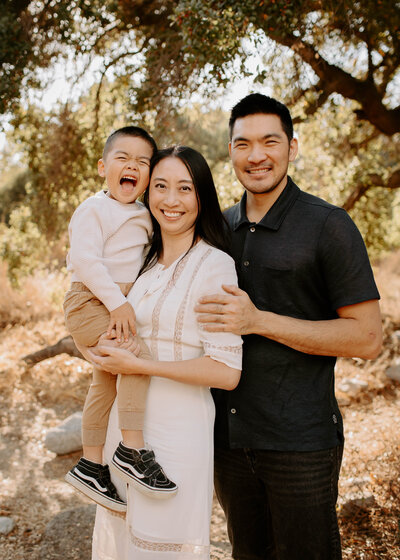 Family of three smiling with their young son laughing loudly during a joyful outdoor family photo session in Pasadena, California. 