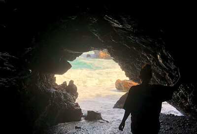girl walking out of a cave into the ocean