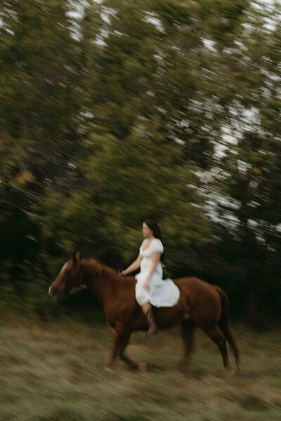 Girl in white riding a brown horse in the summertime