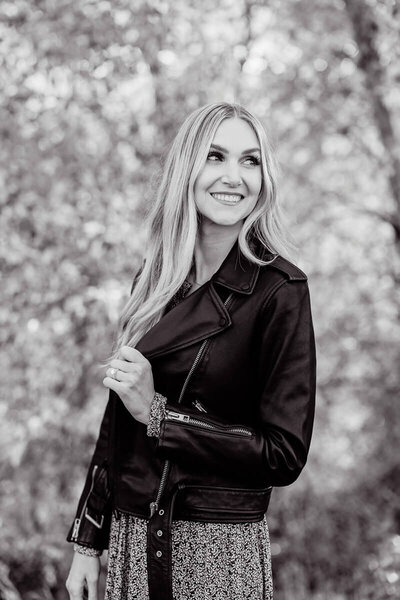 blonde woman in black  leather jacket smiling and looking away from camera