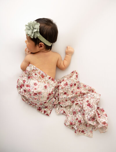 8 day newborn girl lying on stomach, wearing a green bow headband and a lace wrap covering her bottom.