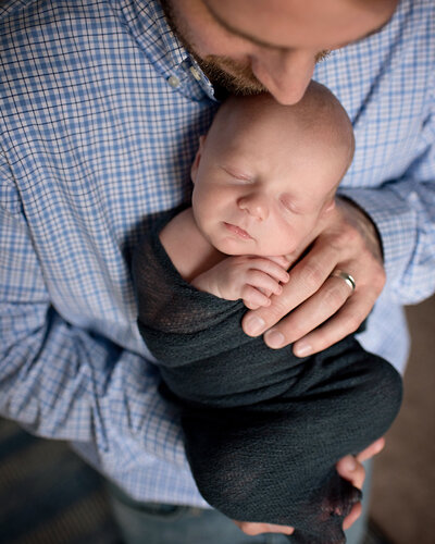 Father holding his newborn son in his hands at a newborn photo shoot in Richardson, TX.