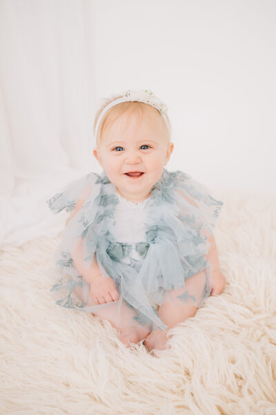 Six month old baby boy smiling at the camera, dressed in white