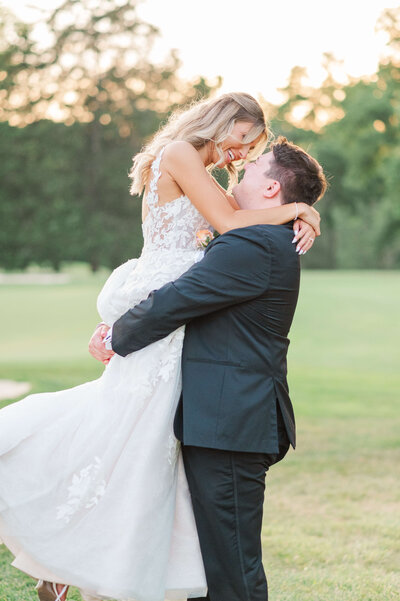 Man holds onto woman and she smiles over her shoulder as the golden sunset is behind them. Taken at a winery in Kentucky by cincinnati based wedding photographer.