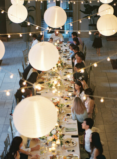 a long dining table with string lights and paper lanterns overhead