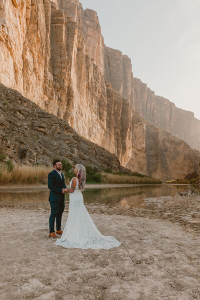 Bride and groom holding hands by the river at St. Elena Canyon in Big Bend National Park, Texas, with towering canyon walls in the background during their intimate elopement.