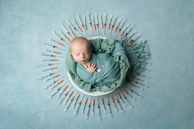 Newborn baby boy swaddled in blue surrounded by a sunburst display of IVF needles