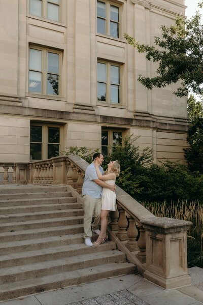 A couple shares a laugh as they snuggle close with beautiful architecture backdrop. 