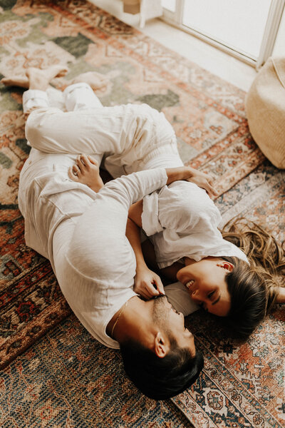 Couple in white lay on bohemian rug looking into each others eyes