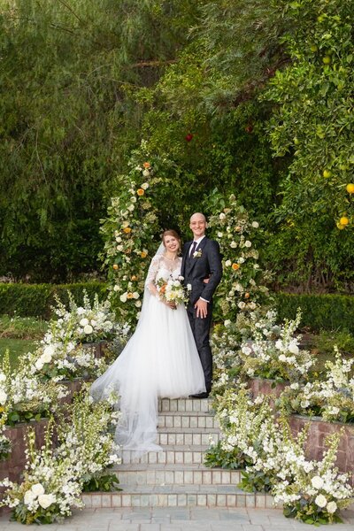 Bride and groom stand in front of a whimsical white ceremony arch installation at Newhall  Mansion