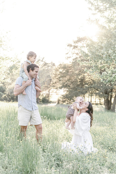 A family of 4 play in a field at sunset by Nashville Newborn Photographer Kristie Lloyd