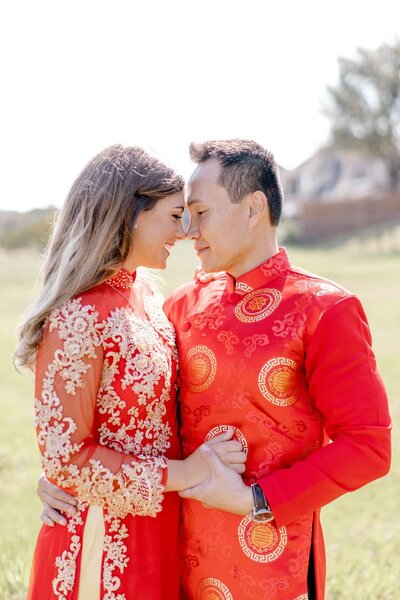 bride and groom in bright red attire hold their heads close in an embrace