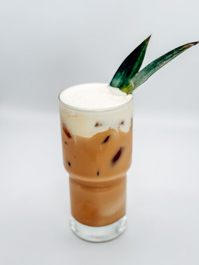 Piña Colatte specialty iced latte from Quigley Coffee Co, topped with cold foam and garnished with a pineapple leaf.
