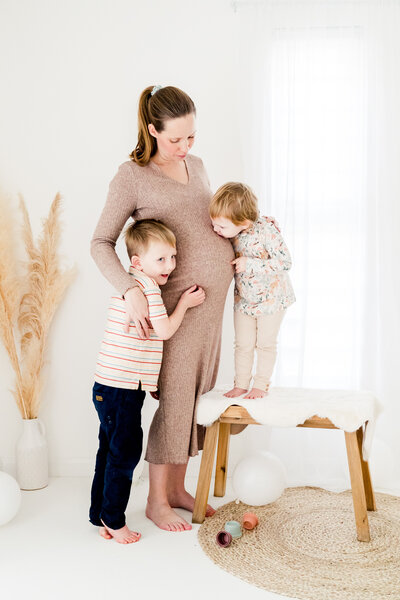 a wicker bassinet stands in the corner of a beautiful white photography studio next to pampas grass