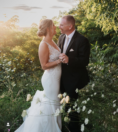 A bride and groom embracing surrounded by trees and flowers.