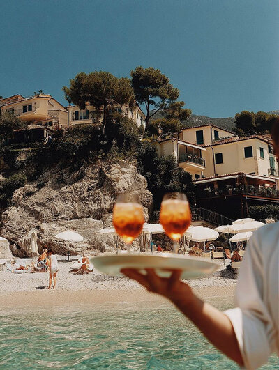 Savoring Aperol Spritz with sun on your face and the European coast stretching below a cliffside villa. Tailored Oasis Travel Co.