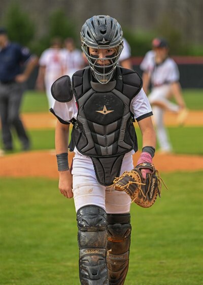 a catcher walks toward the camera in a middle school baseball photo 