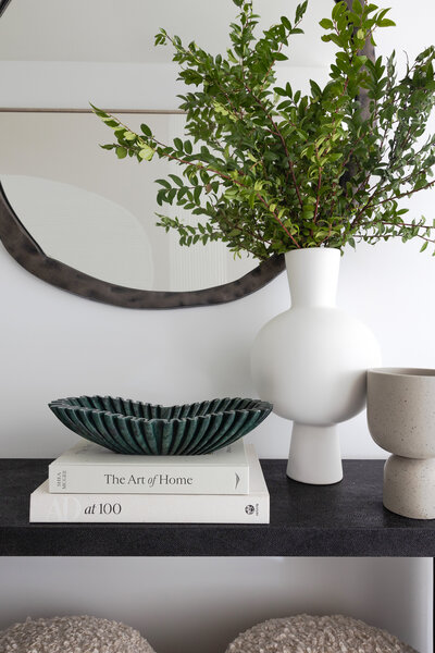 living room decor. terracotta decorative bowl, greenery and vases. circular mirror. design books