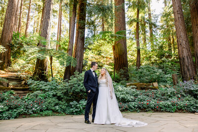 Bride and groom at Nestldown  in their wedding attire during their couple's portraits before they get married. The  tall trees of the estate are the backdrop of their images.