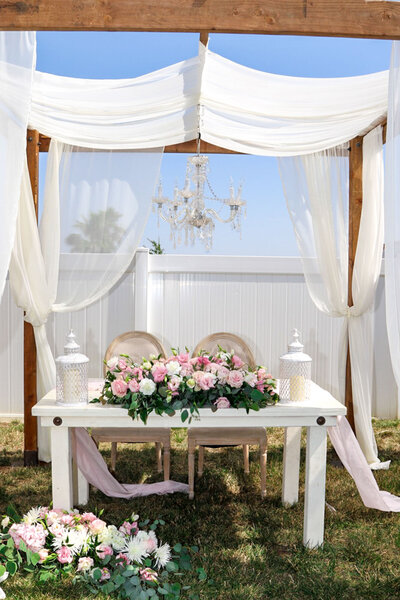 Outdoor sweetheart table setup under a white draped pergola