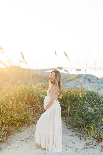 Pregnant mother holding her belly and smiling at the camera at sunrise