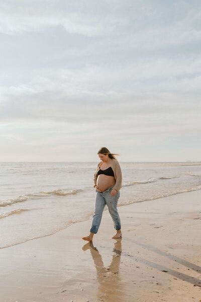 Mother showing bump and walking along a beach