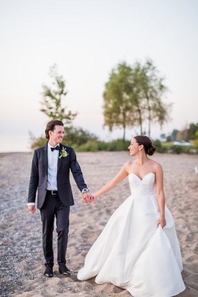 Bride and groom holding hands walking along the beach during sunset