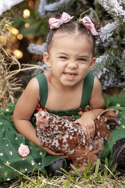 young child smiling in a green dress holding a chicken