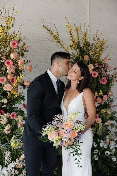 Couple kissing in front of floral set up designed by Helena Elizabeth Events, wedding planner brooklyn