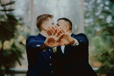 Close-up of two grooms with one showing henna tattoo on his hand.