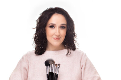 woman wearing pink top holding makeup brushes and smiling