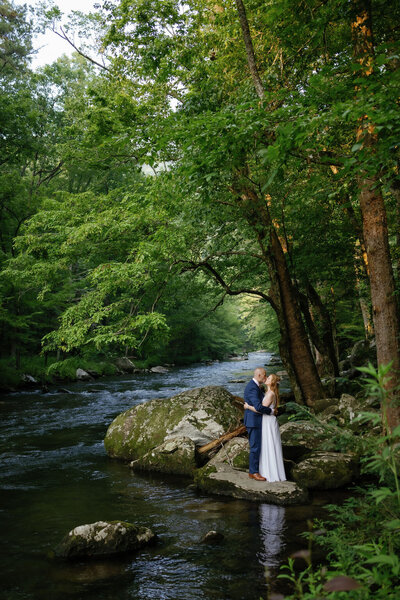 woodland elopement in the Smoky Mountains with bride and groom embracing on a stone in a river in the woods captured by photographers in gatlinburg tn while the couple elopes to Gatlinburg 