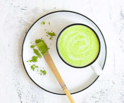 Green matcha latte in a white mug with bamboo scoop and powder – a nourishing energy boost for perimenopause