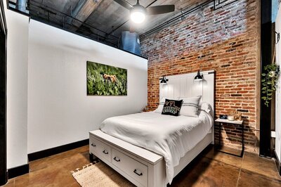Bedroom with Queen bed and exposed brick in this three-bedroom, two-bathroom industrial modern loft condo in the historic Behrens building in downtown Waco, TX.